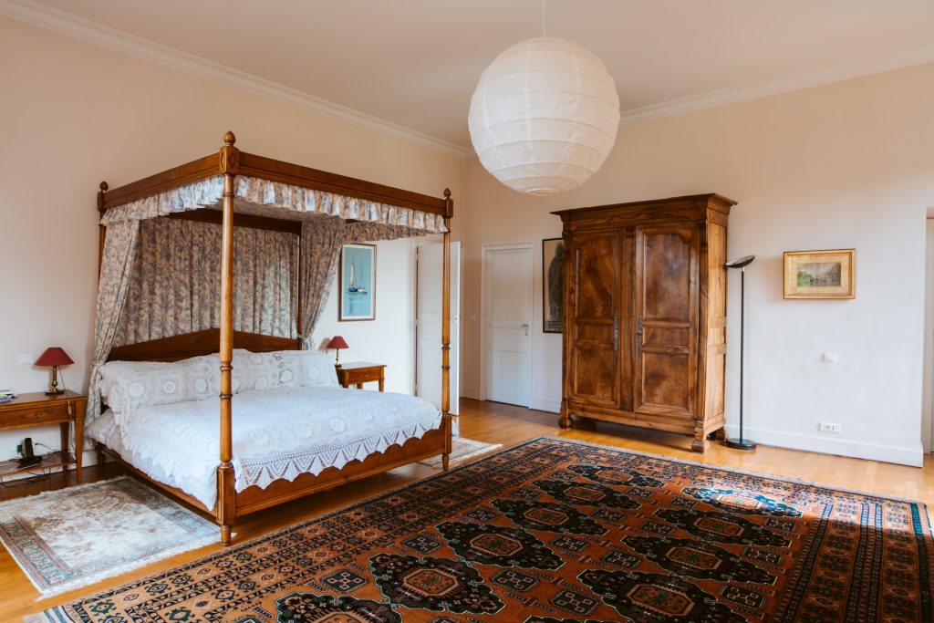 A spacious bedroom with King size four poster bed and wooden wardrobe. On the floor there are multiple colourful rugs