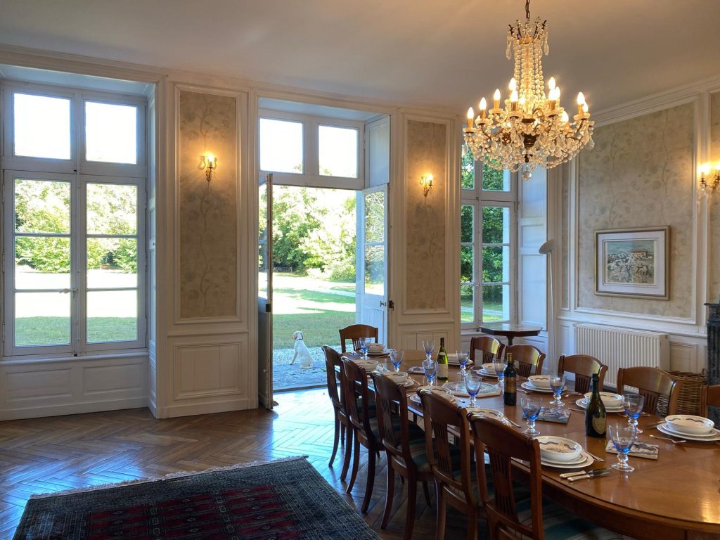 a bright and spacious dining room with long wooden table set for dinner with wooden upholstered chairs